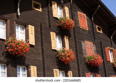 Mountain Village Disentis With Beautiful Wooden Facade And And Red Flowers On A Blue Cloudy Late Summer Day. Photo Taken September 5th, 2022, Rueras, Switzerland.