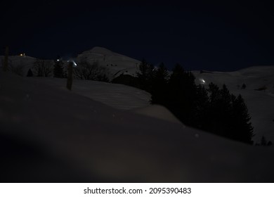 Mountain village Stoos by night with slope and illuminated snow canons spraying artificial snow with mountain panorama in the background. Photo taken December 20th, 2021, Stoos, Switzerland.