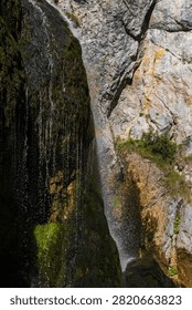 Mountain waterfall cascading down a steep rocky cliff face with green moss in a deep alpine canyon in Austria