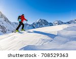 Mountaineer backcountry ski walking up along a snowy ridge with skis in the backpack. In background blue sky and shiny sun and Zebru, Ortler in South Tirol, Italy.  Adventure winter extreme sport. 