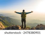 Mountaineer with backpack on shoulders on top of mountain with arms outstretched, travel, mountaineering concept