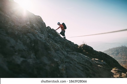 Mountaineer with backpack using climbing rope to climb rocky mountain - Shutterstock ID 1863928066