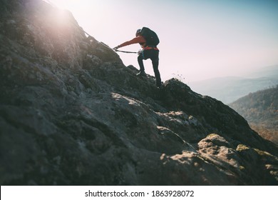 Mountaineer climbing rocky summit. Climber reaching top via ferrata - Shutterstock ID 1863928072