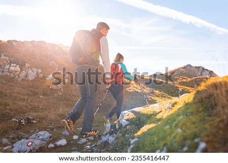 Mountaineer couple with backpacks and trekking poles doing a high mountain route on a nice sunny day. Seasonal vacation concept.