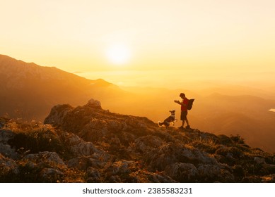 Mountaineer man with backpack plays with his border collie dog while hiking in the mountains at sunset. Mountain sports and adventure - Powered by Shutterstock