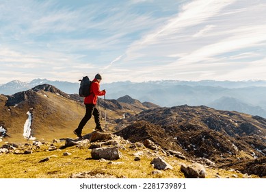 mountaineer man from behind with red clothes, backpack and trekking poles practicing high mountain hiking. outdoor sport and adventure. - Powered by Shutterstock