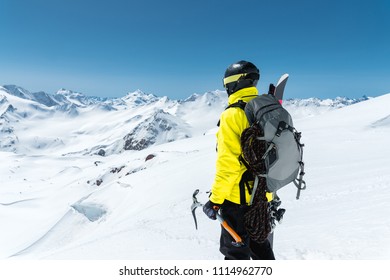 A Mountaineer Man Holds An Ice Ax High In The Mountains Covered With Snow. View From The Back. Outdoor Extreme Outdoor Climbing Sports Using Mountaineering Equipment