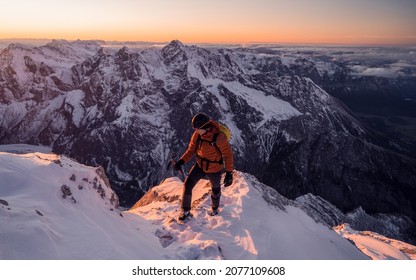 Mountaineer on the top of a mountain in the background of the landscape of snowy mountains during sunrise or sunset. Climber on a summit freedom