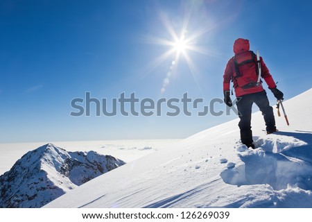 Mountaineer reaches the top of a snowy mountain in a sunny winter day. Western Alps, Biella, Italy.