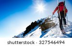 Mountaineer walking up along a snowy ridge with skis in the backpack. In background blue sky and shiny sun. Concepts: adventure, determination, extreme sport. Large copy-space on the left for text.