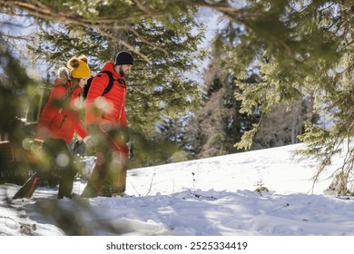 Mountaineering couple hike through a snowy forest with mountains in background, winter season - Powered by Shutterstock