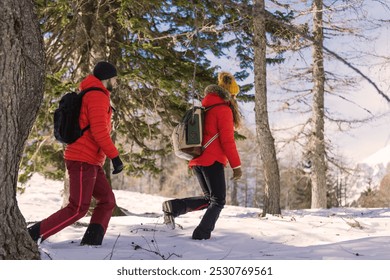 Mountaineering couple hike through a snowy forest with mountains in background, winter season - Powered by Shutterstock