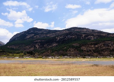 A mountainous landscape with sparse trees and a small settlement near a body of water.