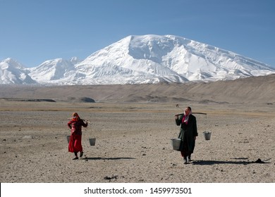 Mountainous landscape. Two Kyrgyz women with buckets of water on a yoke on the background of Muztagh Ata mountain (7546 m). Pamir mountains, outskirts of Kashgar, Xinjiang, China, Asia. - Shutterstock ID 1459973501