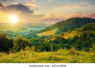 mountainous rural landscape at sunset. beautiful scenery with forests, hills and meadows in evening light. ridge with high peak in the distance. village in the distant valley