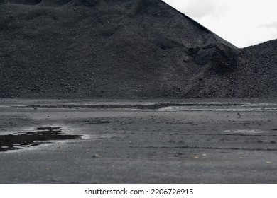 Mountains Of Black Coal In A Concept Of Energy Crisis And Energy Shortage In The Foreground Puddles With Grey Sky