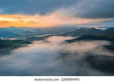 Mountains in clouds at sunrise in summer. Aerial view of mountain peak with green trees in fog. Beautiful landscape with high rocks, forest, sky. Top view from drone of mountain valley in low clouds - Shutterstock ID 2280984991