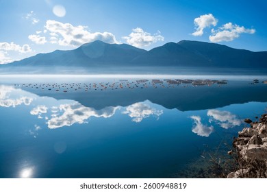 Mountains with clouds and their reflection in the still waters of the sea, separated by a strip of fog in winter morning Bay of Kotor in Montenegro. High quality photo