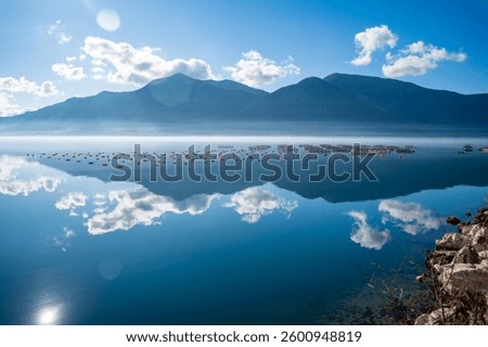 Mountains with clouds and their reflection in the still waters of the sea, separated by a strip of fog in winter morning Bay of Kotor in Montenegro. High quality photo