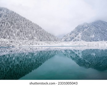 Mountains covered with trees and snow are symmetrically reflected in the turquoise water of the lake. Winter landscape. - Powered by Shutterstock