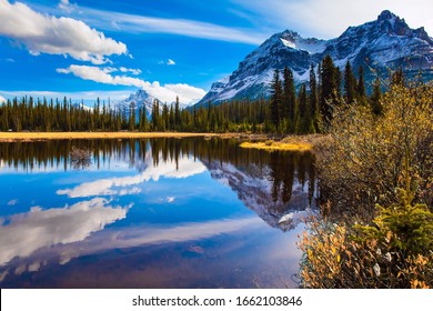 The mountains, forests and lake in the Rockies of Canada. Clouds reflected in the smooth water of the lake. Autumn trip to the Rockies of Canada. The concept of active, eco and photo tourism