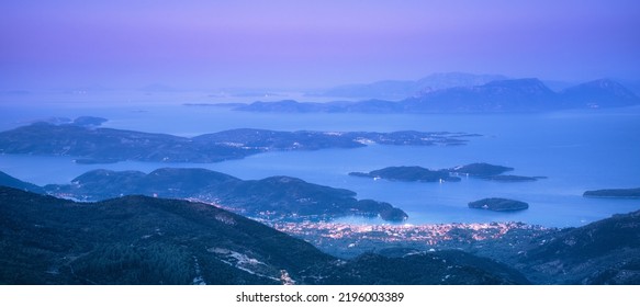 Mountains, islands and city on the sea cost at night. Aerial view. Landscape with city lights, port, town, buildings, forest on hills, blue water and purple sky at dusk. Greece. Travel and nature - Powered by Shutterstock