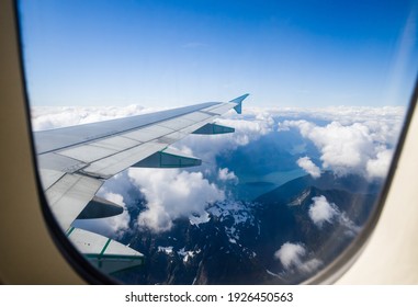 mountains, lakes and rivers outside a plane window. Travel time, sky, clouds and plane wing. Aerial view