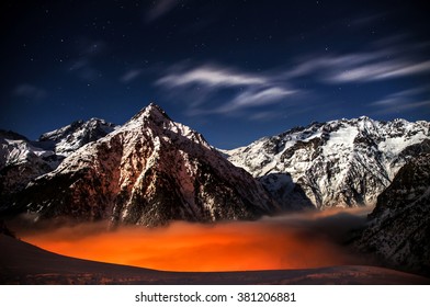 Mountains in the moonlight with orange-red clouds and a village under them - Shutterstock ID 381206881