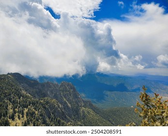 Mountain-top view at the peak with dramatic clouds, vibrant blue skies, and forested mountains