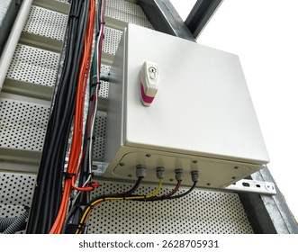 Mounted electrical control box with labeled lock and connected multicolored cables, installed on a perforated metal panel alongside bundled wiring and a ladder-like cable tray