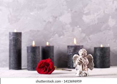 Concept de deuil. Petit ange, fleur de rose rouge clair et bougies en feu sur fond gris texturé. Carte de deuil, de mort, de chagrin.Mise au point sélective. Placez le texte.