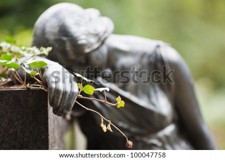 mourning female sculpture as a gravestone on a cemetery holding an ivy branch and a wilted rose in her hand