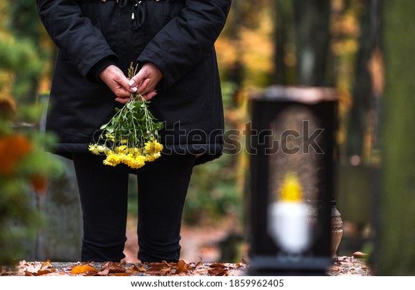 Mourning woman holding flowers in\
hands and standing at grave in cemetery. Sadness during\
funeral