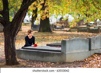 Mourning Woman Laying Flower on Grave in Cemetery in Fall