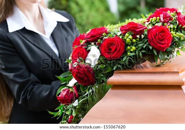 Mourning woman on funeral with red rose standing\
at casket or coffin