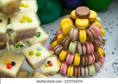 Mousse in glasses and colorful french macarons multilevel cake pyramid on plastic dessert stand.
