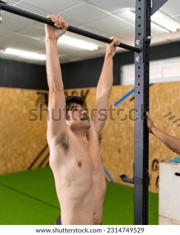 Moustached, shirtless young man in good physical shape gripping the top bar of the training box before starting the exercise at the training center.