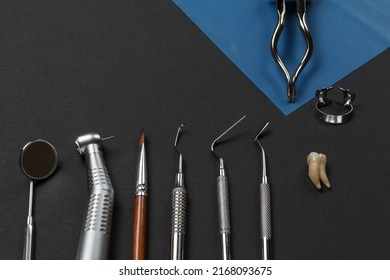 Mouth mirror, a dental handpiece, a brush, a curette, a plugger, a dental restoration instrument and a rubber dam clamp pliers with clamps and an extracted sick tooth. Medical tools. Top view.