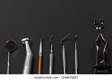 Mouth mirror, a dental handpiece with bur, a brush, a curette, a plugger, a dental restoration instrument, a rubber dam clamp pliers with a clamp on the black background. Medical tools. Top view.