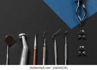 Mouth mirror, a dental handpiece with bur, a brush, a curette, a plugger, a dental restoration instrument and a rubber dam clamp pliers with clamps on the black background. Medical tools. Top view.