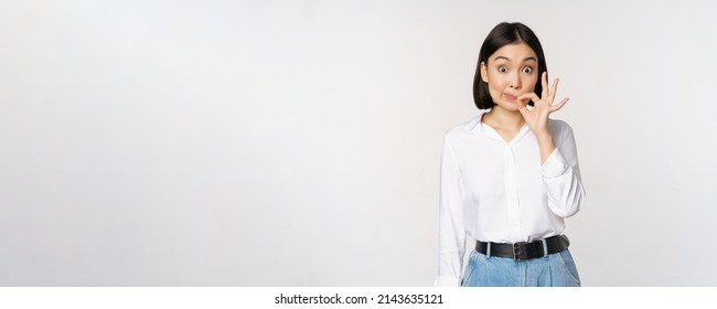 Mouth shut. Young asian woman seal lips, showing taboo dont speak, keep quiet sign, hiding secret, standing over white background
