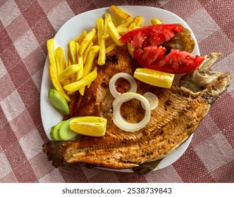 mouthwatering plate of grilled fish, served with a side of crispy French fries, fresh tomato slices, and a lemon wedge. Golden brown crust and is garnished with onion rings. Traditional restaurant - Powered by Shutterstock