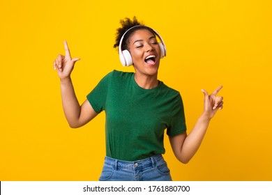Move Your Body. Portrait of smiling afro girl listening to music in headphones with closed eyes, dancing and pointing up