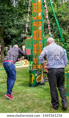 Movement is blurred as a man swings the hammer with enough force to ring the bell at the top. A 'high striker', 'strength tester', or strongman game is a typical english fairground attraction.
