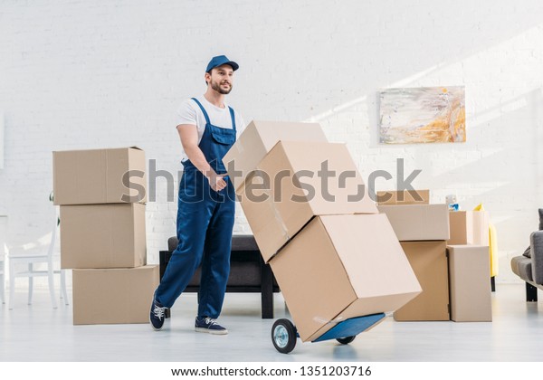 mover in uniform transporting  cardboard boxes\
on hand truck in\
apartment