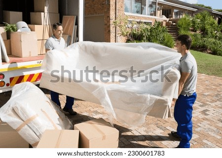 Movers carrying sofa from moving van in driveway