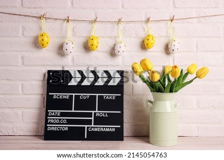 Movie clapper board with Easter decorations against a white brick wall. Cinema for the spring holidays. 