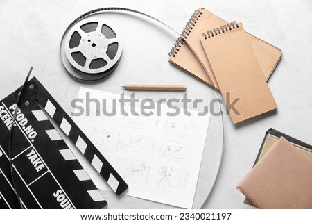 Movie clapper with storyboard, notebooks and film reel on light background