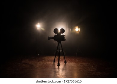 Movie Concept. Miniature Movie Set On Dark Toned Background With Fog And Empty Space. Silhouette Of Vintage Camera On Tripod. Selective Focus