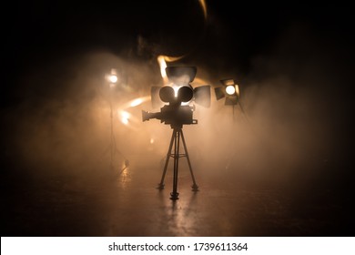 Movie Concept. Miniature Movie Set On Dark Toned Background With Fog And Empty Space. Silhouette Of Vintage Camera On Tripod. Selective Focus